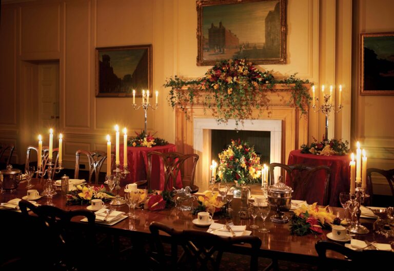 A long wooden dining table decorated with floral arrangements and numerous glowing candles.
