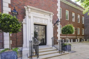 The front entrance of a large red brick building. There is a short stone staircase leading up to the black front door.