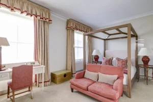 A large bedroom with a peach coloured sofa at the foot of a large four poster bed.
