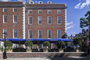 Exterior of the red brick Inner Temple building with rows of sash windows, blue Pegasus awning, and neatly trimmed trees along the pavement.