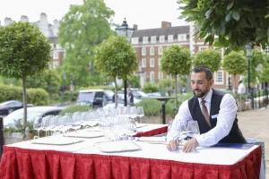 A waiter setting placing wine glasses on an outside table in summer.